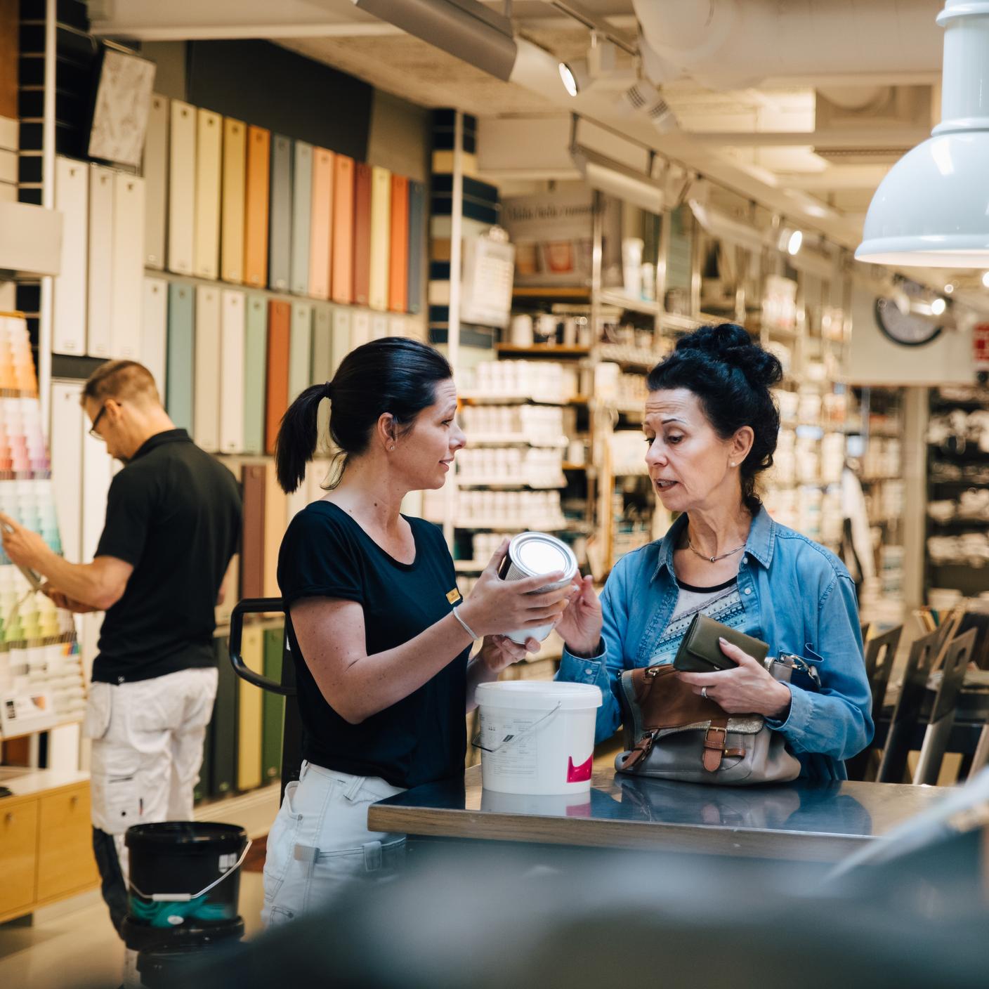 Sales woman showing paint can to customer at hardware store