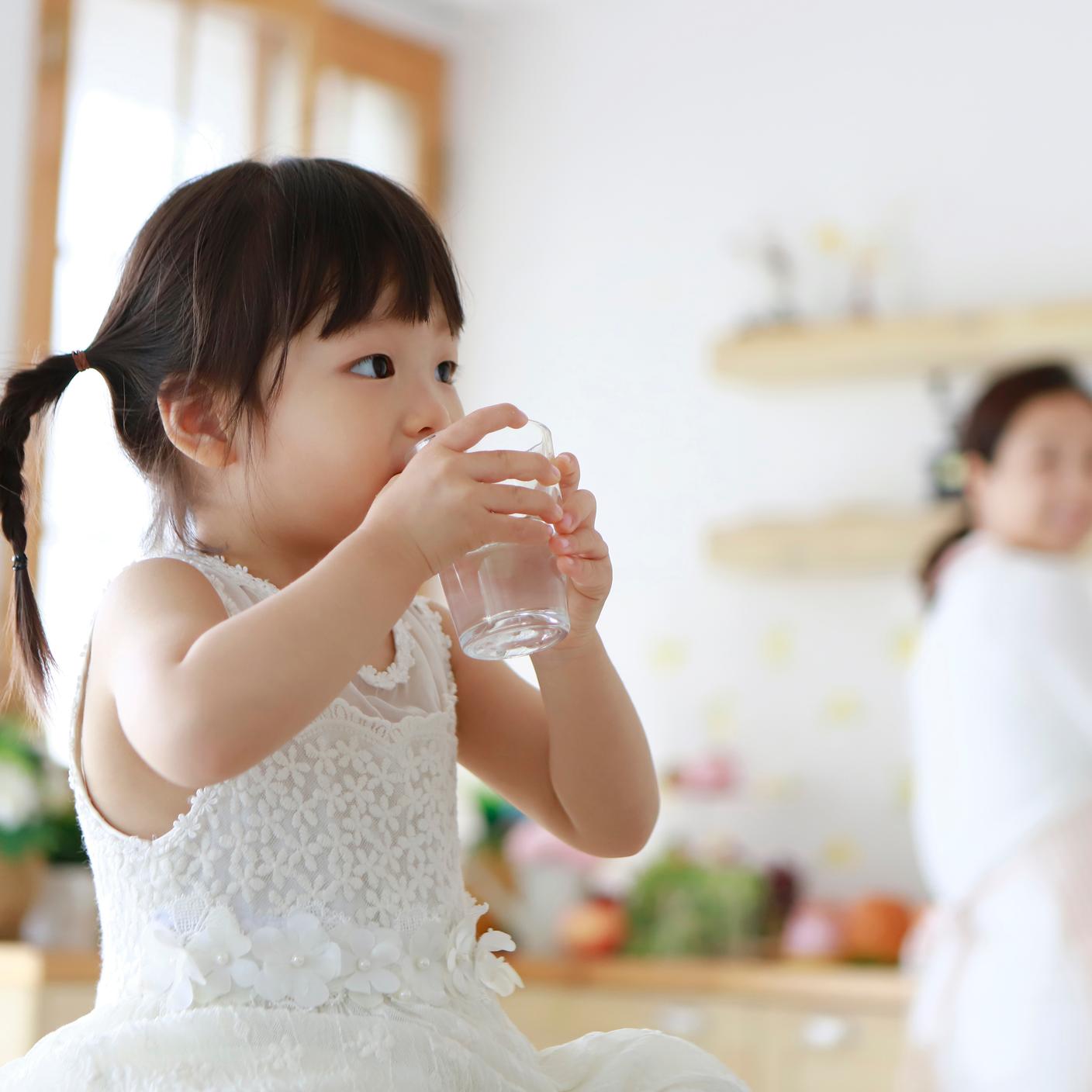 Little girl drinking glass of water in kitchen