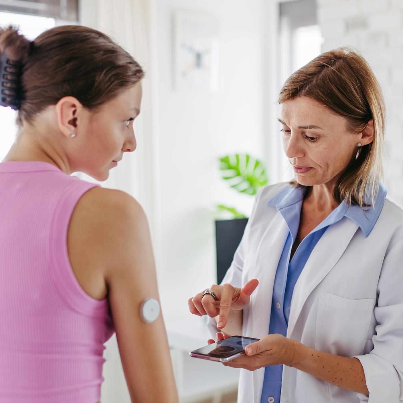 Diabetologist connecting the smartphone to the continuous glucose monitor on teenage patient's arm