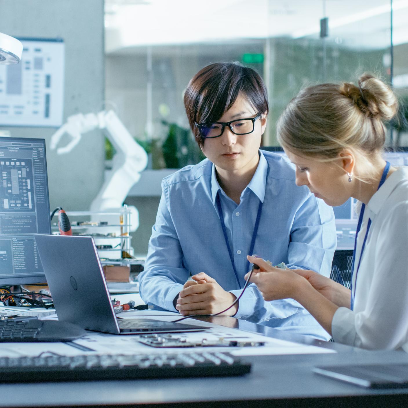 Asian Scientist Sitting at His Desk Consults Engineer 