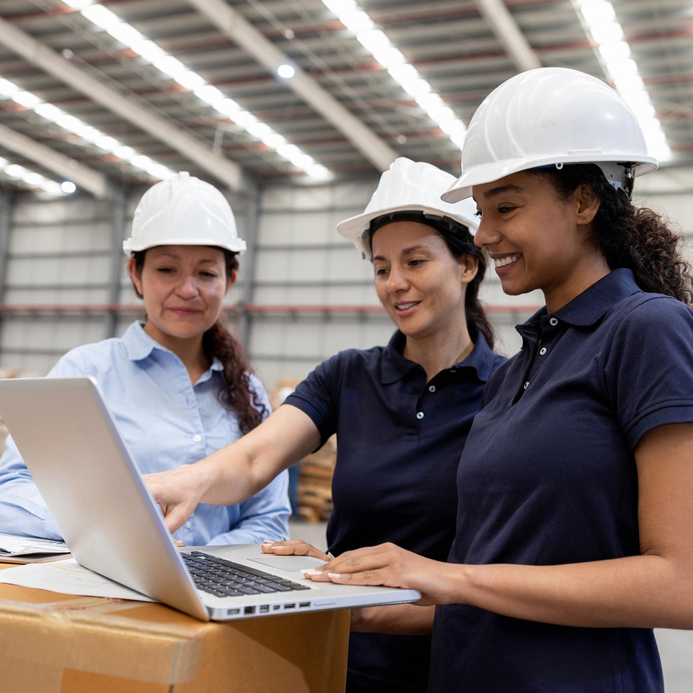 Team of women working at a distribution warehouse coordinating the logistics of shipping using a laptop computer