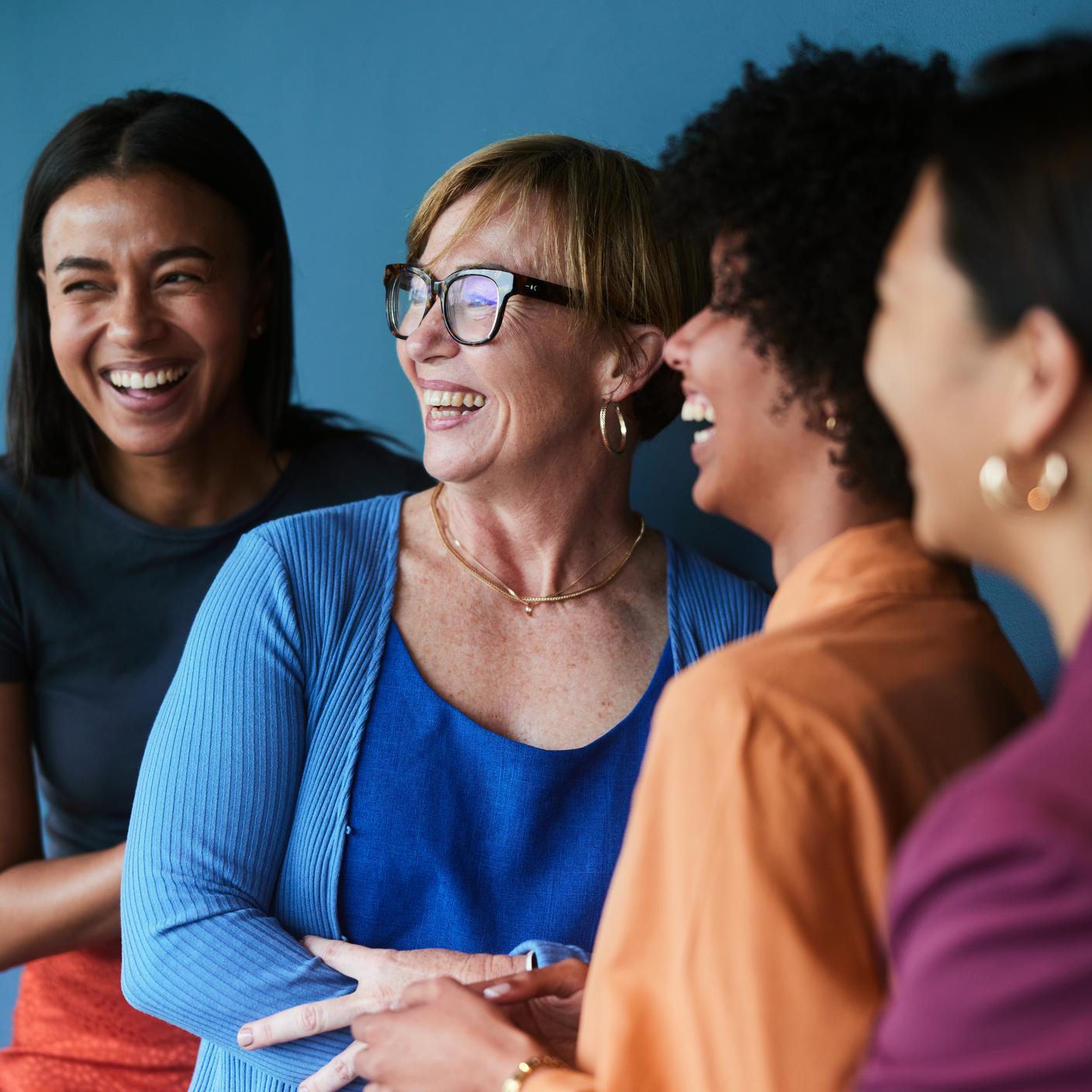 Group of diverse businesswomen laughing while standing together in front of a blue background