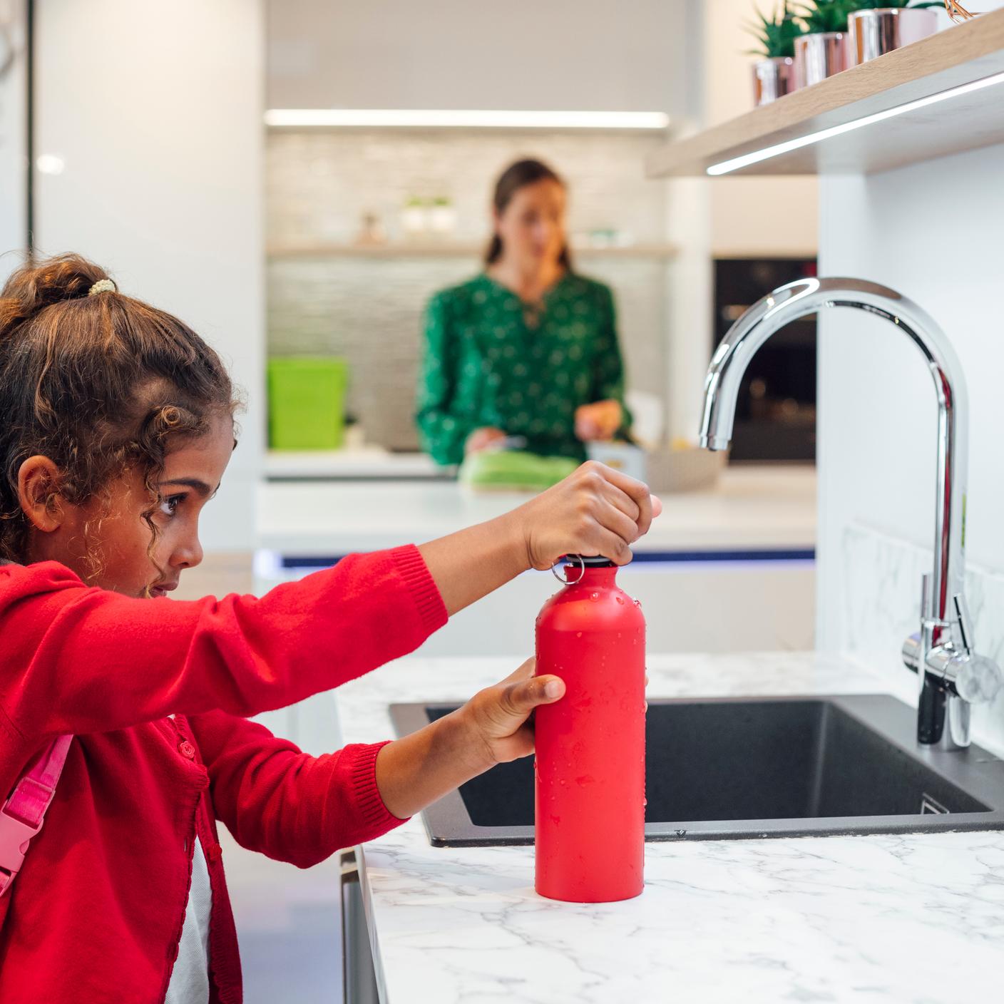 A young schoolgirl in her uniform fills up her water bottle before heading to school.