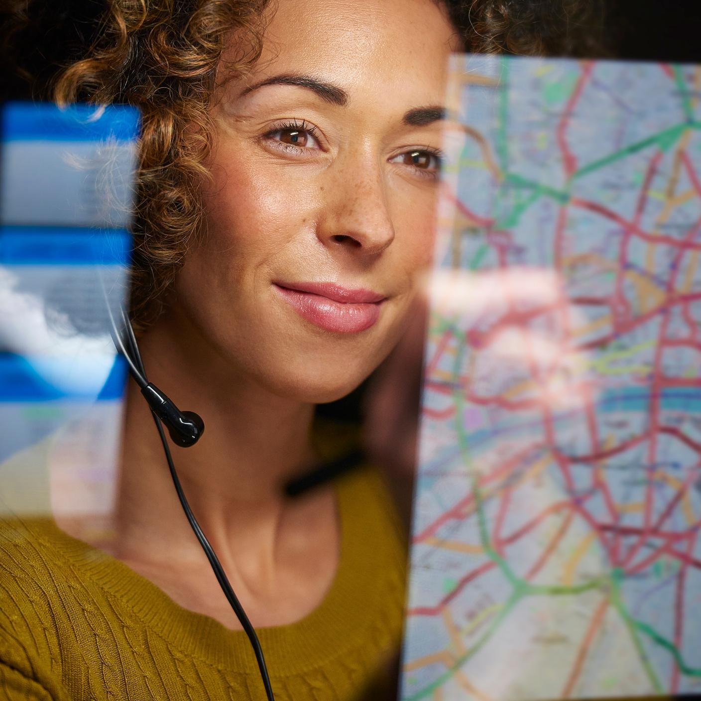 A female logistics worker is organising dispatch of freight on her interactive digital map whilst talking on her headset.